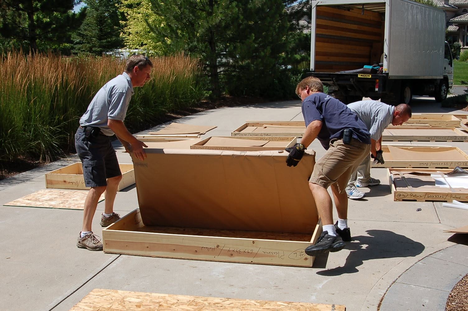 Three Specialized Moving Services technicians positioning a protected item inside a custom wood crate on-site